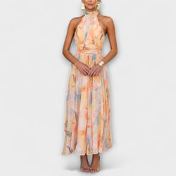 A female model wearing a halter neck, open back, watercolour print maxi dress.