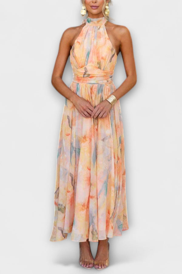A female model wearing a halter neck, open back, watercolour print maxi dress.